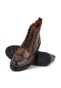 Brown leather ankle boots with brogue detailing, flat black rubber sole, round toe, and lace-up design featuring a side zipper for easy wear.