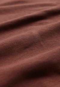 Tela suave y acanalada en un tono marrón oscuro, mostrando una textura lisa con sutiles variaciones de luz y sombra a lo largo de la superficie.