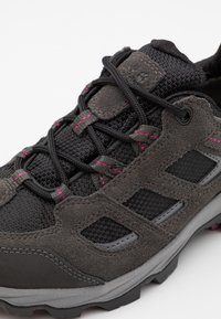 Grå vandringsko med nät- och mockadelar, rosa sömmar, texturerade snören och en robust gummisula för grepp. Hållbar design.