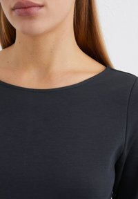 Donkergrijs, getailleerd topje met een ronde halslijn. Smooth textuur met een minimalistisch ontwerp. Geen patronen of hardware zichtbaar.
