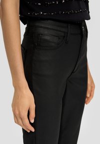 Czarne dżinsowe spodnie z pięcioma kieszeniami, gładką teksturą i dopasowanym krojem. Pas wyposażony jest w szlufki na pasek oraz subtelne detale w szwie.