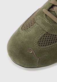 Green suede shoe with mesh accents, featuring a prominent embroidered Puma logo on the side and textured laces.