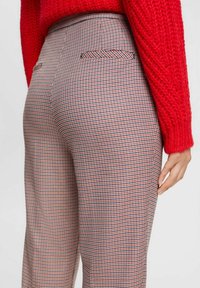 Rutig byxor i röd, svart och vit mönster; rak benform; har två bakfickor; tyget verkar slätt och strukturerat.