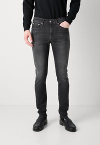 Jeans skinnies negros con un acabado desgastado, cinco bolsillos y detalles sutiles de costura, combinados con mocasines negros.