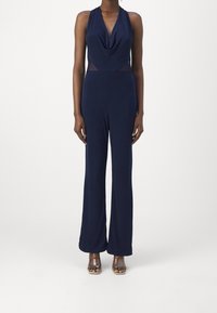 Marinblå jumpsuit med draperad halsringning, figurnära midja och utsvängda ben; tillverkad av ett smidigt, stretchigt tyg; har genomskinliga sidopaneler.