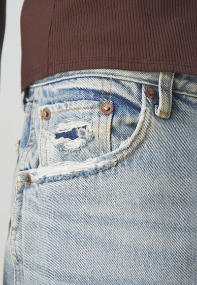 Lichtblauwe ver distressed denim jeans met franje randen en een zichtbare patch op de zak. Vijf-pocket ontwerp met bronzen metalen hardware.