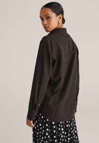 Mustast pikast varrukast särk kraega, nööpidega varrukaotstega, siledat tekstuuri ja lõdva lõikega, millele on lisatud täpiline seelik.