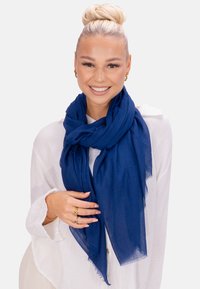 Écharpe bleu marine en tissu léger et texturé, drapée élégamment autour du cou, avec des bords frangés.