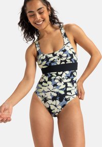 Maillot de bain une-pièce avec un motif floral dans des nuances de bleu, vert et noir, avec une large bande noire à la taille et un décolleté en forme de scoop.