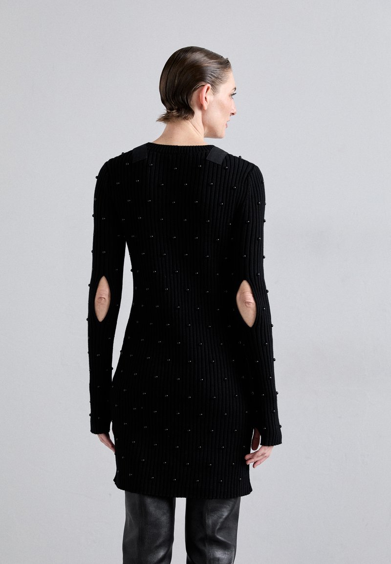 Robe noire en tricot côtelé avec des manches découpées, ornée de petites perles noires et d'accents sur les épaules, arrivant jusqu'au mi-thigh.