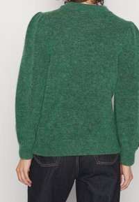 Grön stickad tröja med en texturerad yta, med puffärmar och rundad hals. Designen är figursydd vid midjan och har ribbade muddar.