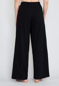 Mustat leveät housut, jotka on valmistettu pehmeästä ja venyvästä kankaasta. Varustettu joustavyötäröllä, täydellä pituudella ja yksinkertaisella muotoilulla ilman kuvioita tai korostuksia.