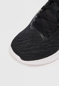 Svart atletisk sneaker med en teksturert mesh-overdel, snøring og en hvit gummisåle. Subtilt mønster gir visuell interesse.