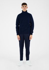 Maglione a collo alto navy in un knit testurizzato, abbinato a pantaloni navy sartoriali e sneakers bianche. Design semplice e aderente con accenti a coste.