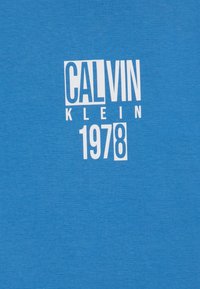 Camiseta de algodón azul con un logo gráfico blanco que incluye el texto "CALVIN KLEIN 1978". Diseño simple, textura suave, mangas cortas.