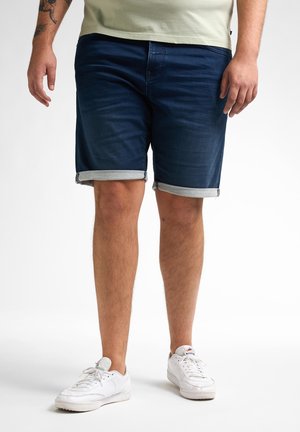 Dunkelblaue Jeansshorts mit umgeschlagenen Säumen, im klassischen Schnitt und mit Fünf-Taschen-Design. Kombiniert mit weißen Sneakers.