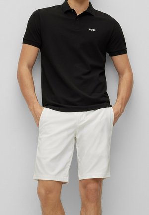 Zwart poloshirt met korte mouwen, voorzien van een geknoopte kraag en een klein wit "BOSS"-logo. Gecombineerd met witte getailleerde shorts.