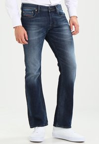 Mörkblå denimjeans med rak passform, blekt utseende, fem fickor och mässingsknappsdetaljer, kombinerat med vita sneakers.