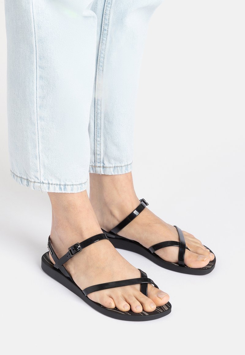 Schwarze flache Sandalen mit einem eleganten Design, dünnen Riemen und einer strukturierten Sohle. Die Riemen verfügen über verstellbare Schnallen für eine optimale Passform.