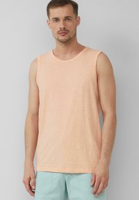 Pfirsichfarbenes, ärmelloses Tanktop aus weichem Stoff mit Rundhalsausschnitt und etwas lockerer Passform. Kombination mit hellblauen Shorts.