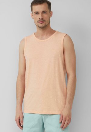 Débardeur sans manches de couleur pêche en tissu doux, avec un col rond et une coupe légèrement ample. Associé avec un short bleu clair.