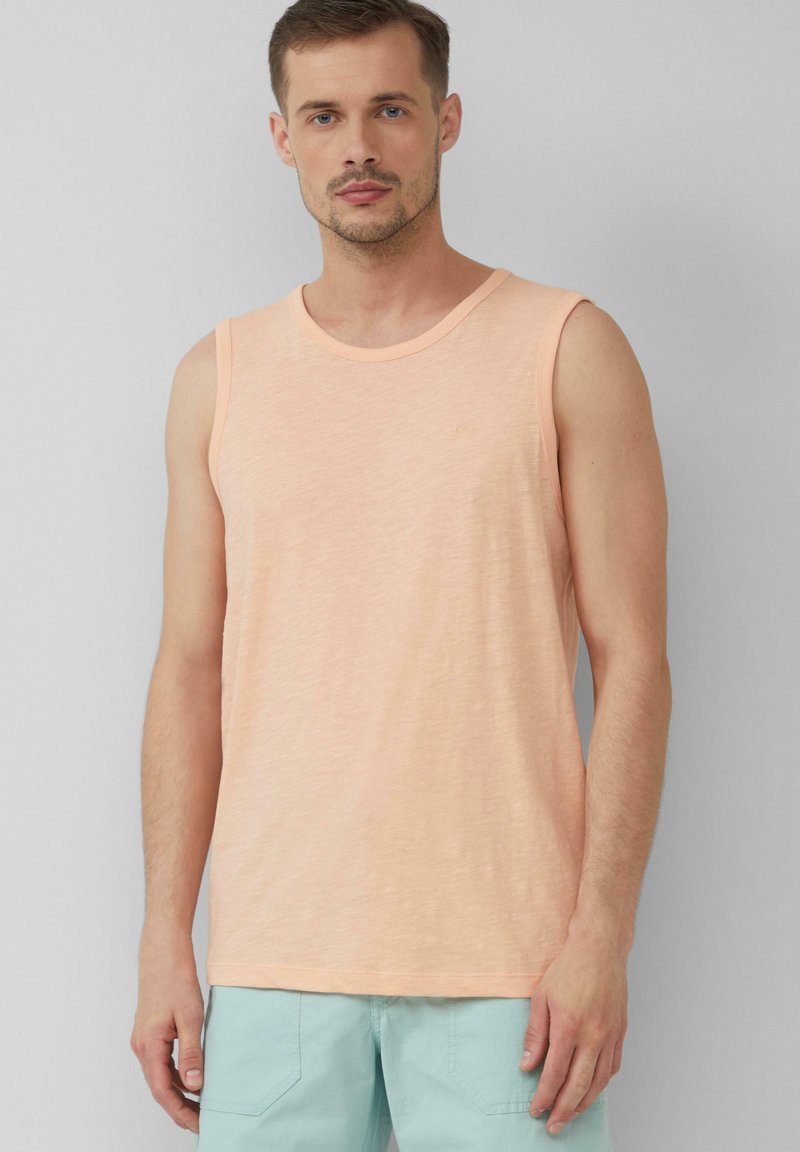 Pfirsichfarbenes, ärmelloses Tanktop aus weichem Stoff mit Rundhalsausschnitt und etwas lockerer Passform. Kombination mit hellblauen Shorts.