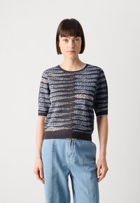 Kortermet genser i mørk grå med et blått og kremfarget bladmønster. Rund hals og ribbestrikket kant, kombinert med lyse denimbukser.