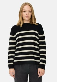 Zwart en crèmekleurig gestreepte trui met geribbelde textuur, ronde hals en brede mouwen. Gecombineerd met donkergrijze broek; minimalistisch ontwerp.