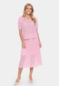 Completo due pezzi rosa in pizzo composto da una maglietta a maniche corte con un motivo a scallop e una lunga gonna coordinata, entrambi con una texture trasparente.