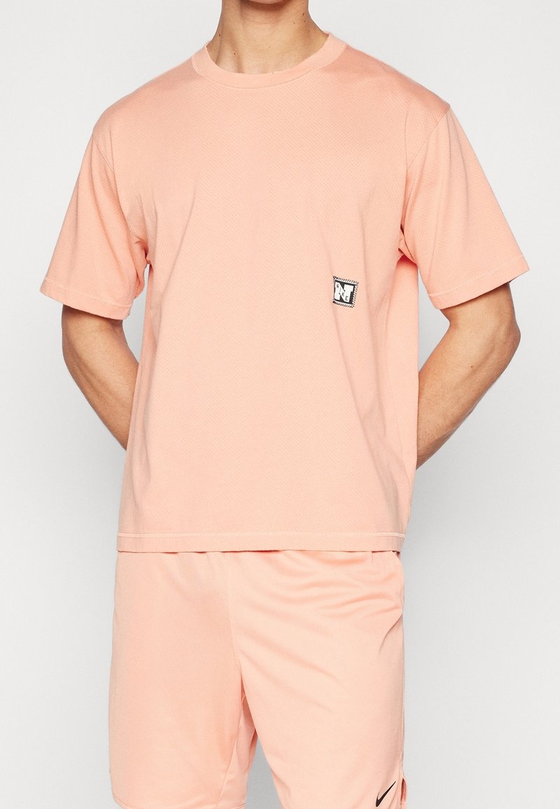 Light pink short-sleeve t-shirt featuring a textured pattern and a small black and white logo patch on the left chest.