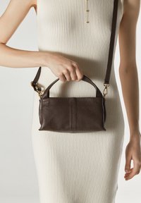 Brązowa skórzana torebka o teksturowanym wykończeniu, z górnym uchwytem i regulowanym paskiem. Złote akcenty hardware'u podkreślają design.