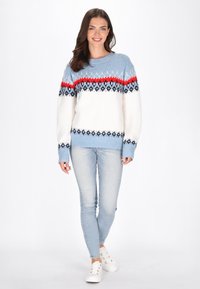 Stickad tröja med en ljusblå övre del, röd rand och geometriska svartvita mönster, tillsammans med ljusblå jeans och sneakers.