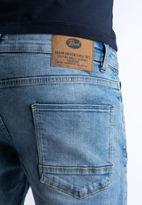 Lichtblauwe denim jeans met een leren label met de tekst "Petrol" op de achterkant. Kenmerken zijn een standaard pasvorm, twee achterzakken en zichtbare stiksels.