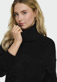 Maglione nero a collo alto realizzato in morbido e soffice tessuto; presenta maniche lunghe e polsini a coste; design minimalista senza motivi visibili.