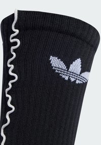 Crna čarapa s rebrastom teksturom, s bijelim čuperkastim rubom i vezenom bijelom Adidas oznakom u obliku tri lista.