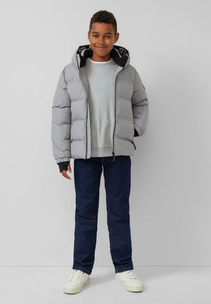 Graue gepolsterte Jacke mit Kapuze, schwarzem Futter und elastischen Bündchen, kombiniert mit einem hellgrauen Sweatshirt und dunklen Jeans. Getragen mit weißen Sneakers.