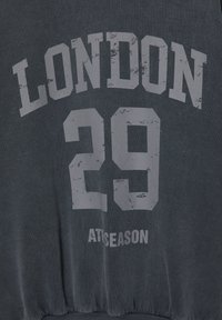 Tummanharmaa collegepaita, jossa on suuret haalistuneet valkoiset kirjaimet "LONDON", alla numero "29" ja alhaalla pienemmällä teksti "ATISEASON".