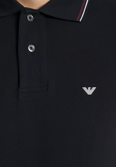 Black polo shirt with a textured fabric, two buttons, and a contrasting collar featuring maroon and white stripes. Small white logo on chest.