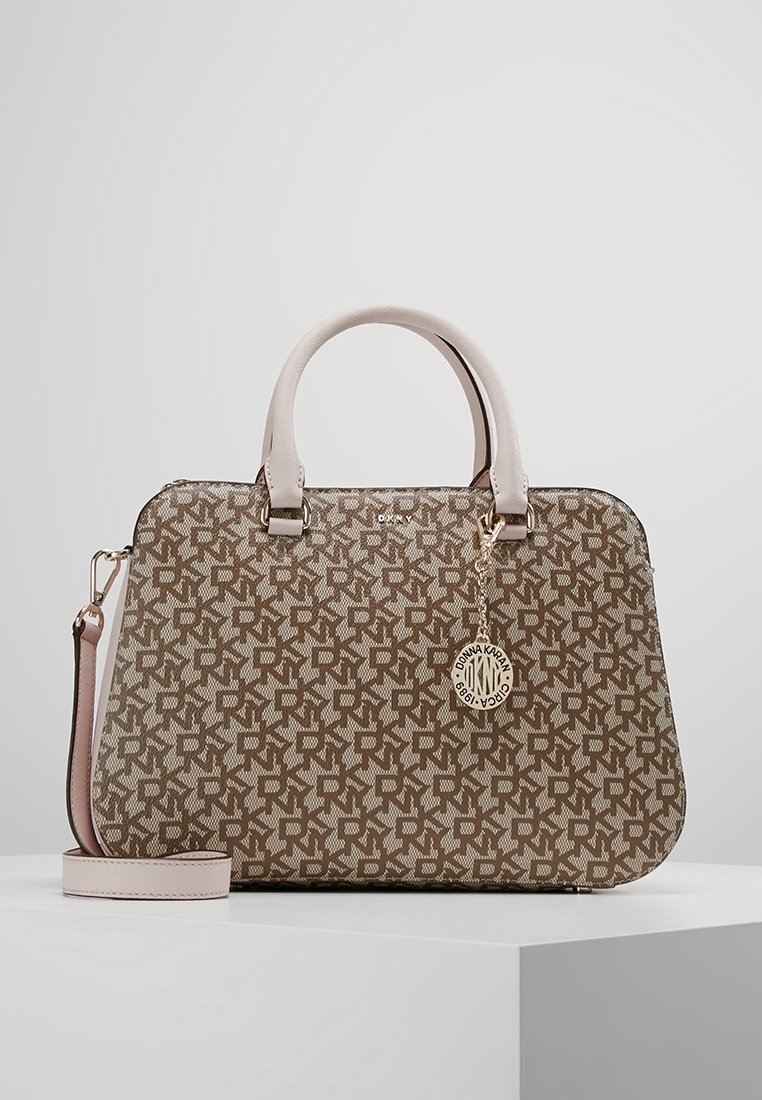 Sac à main DKNY marron et beige à motifs, avec deux poignées, une bandoulière détachable et un pendentif circulaire avec le logo Donna Karan à l'avant.