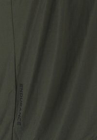 Dunkelgrüner Stoff mit vertikalem Saum und dem Wort „ENDURANCE“, das in dunkler Tinte nahe der Naht aufgedruckt ist.