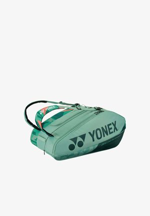 Groene Yonex sporttas met twee met ritsen afgesloten compartimenten en dubbele draagriemen, ontworpen voor het opbergen van rackets en gemakkelijk transport.