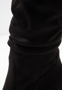 Botín negro de ante hasta el tobillo con una textura suave y un diseño holgado, que presenta detalles de costura mínimos a lo largo del costado.