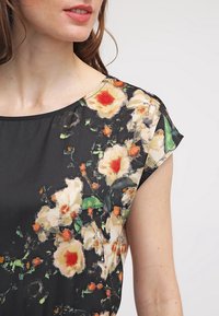 Černá květinová blůza s krátkými rukávy a kulatým výstřihem, zdobená živým potiskem smetanových a oranžových květin s zelenými akcenty.