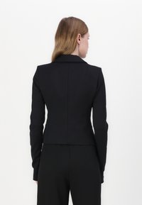 Černé sestavené sako s přiléhavým střihem, klopovým límcem a dlouhými rukávy. Hladká tkanina a minimalistický design bez viditelného hardwaru.