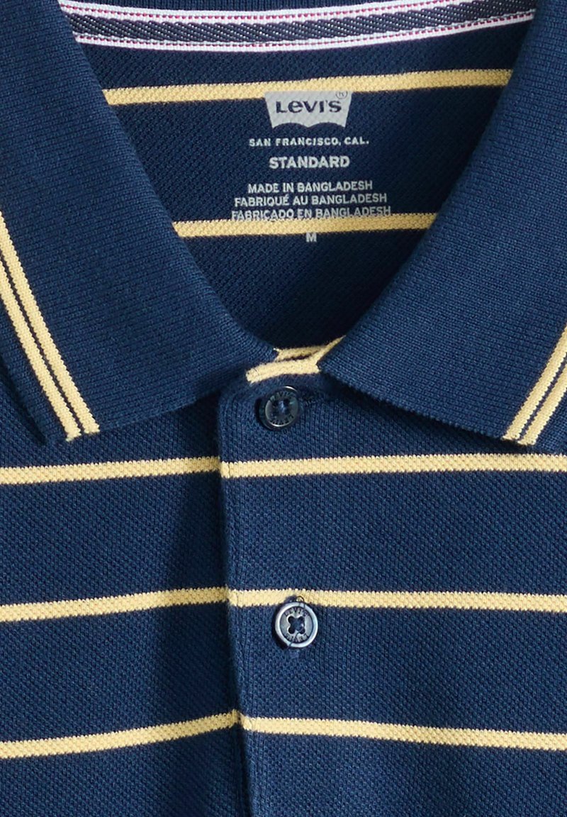 Marineblå Levi's polo med beige horisontale striber, knappet krave, størrelse medium, lavet i Bangladesh.