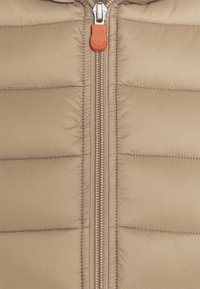 Veste matelassée beige avec un motif matelassé horizontal, dotée d'une fermeture éclair centrale avec un tirette orange et une texture lisse et brillante.