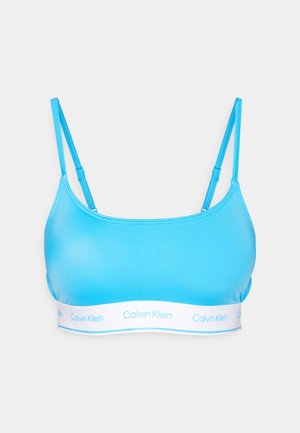 Svijetloplava braleta s podesivim trakama, napravljena od glatkog materijala, s bijelim elastičnim pojasom označenim "Calvin Klein" na dnu.