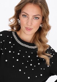 Czarna bluza ozdobiona srebrnymi i perłowymi aplikacjami. Posiada okrągły dekolt z ozdobnym obszyciem z kryształków.