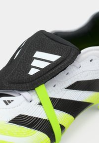 Gros plan sur une chaussure de sport blanche, noire et jaune fluo avec un rabat protecteur noir arborant un logo triangulaire blanc.