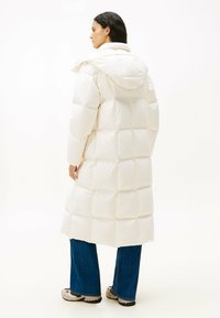 Witte gewatteerde lange jas met een capuchon, met een gewatteerd ontwerp en een zachte textuur. Gepaard met blauwe wijde jeans en beige sneakers.